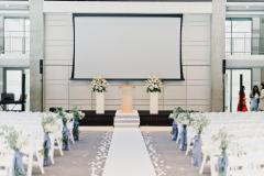 An empty ballroom set for a wedding looking down the aisle at the stage.