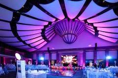 The ballroom set up for an evening event with dining tables, colored lights, and stage and dance floor.