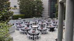 An outdoor courtyard set up for a reception dinner with round tables and chairs.