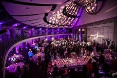A ballroom with purple lighting and full of people celebrating.