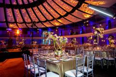 A gold table setting in a ballroom with elegant lighting and a dome-like ceiling.