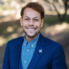 Dr. Yamonte Cooper head shot in a blue collared shirt and blue jacket against a woodsy background.