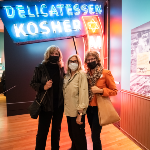 3 women in front of a neon sign that says Delicatessen Kosher