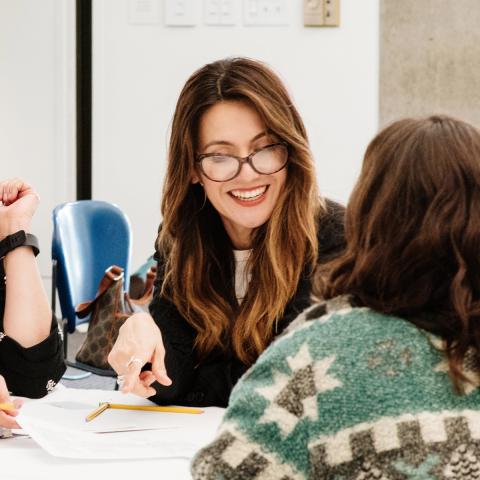 Four women sitting around a table in a class talking to one another