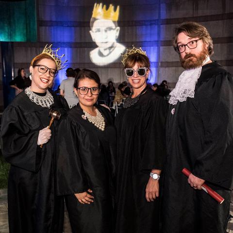 Three women and one man dressed up in Supreme Court robes at a RBG event. Two are wearing crowns.