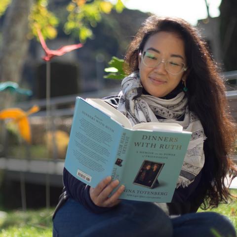 Woman reading a book outside with white patterned scarf on