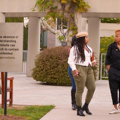 Photo of a group of people walking outside on the Skirball campus. In the foreground an artwork with the words, "In the absence of understanding, a minute can stretch to contain unlimited observations."