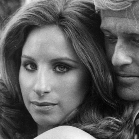 Still from the film showing Streisand and Redford standing together. She is looking at the camera and he is looking down.