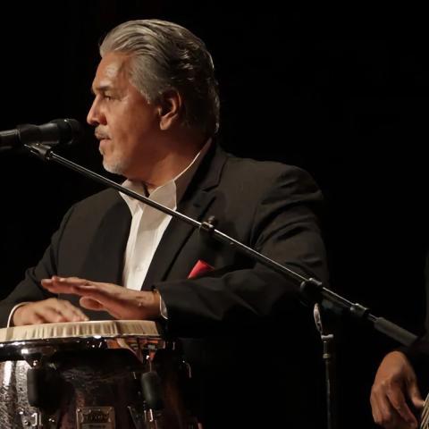 Photo of the artist on a dark stage playing his instrument with another musician behind him.