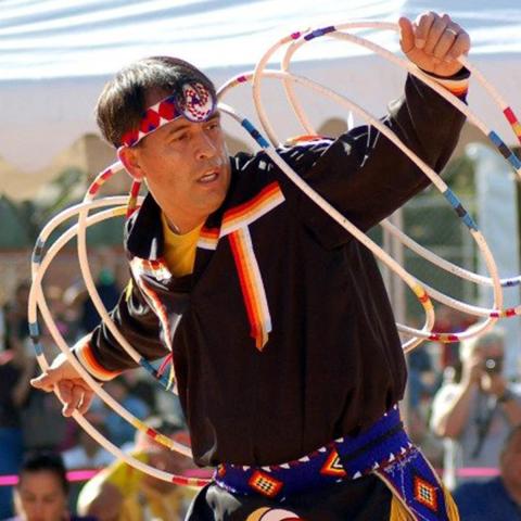 Photo of a man performing outside with numerous hoops moving around his arms