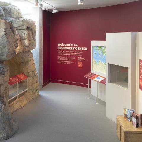 Photo of a artifact gallery with cases and a large rock ancient tomb with a big text wall that reads Discovery Center
