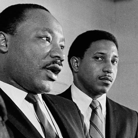 black-and-white photo of two African-American men dressed in suits and standing in front of microphones