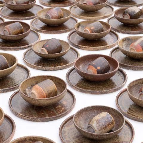 A pattern of a plate, bowl, and cup stacked and put in rows. The dishes are made of brown earthy pottery.