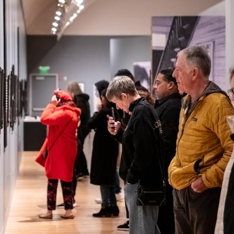 A large group of people standing in a line looking at a long wall of photos