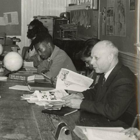 A black and white historic photo of a college scholar sitting at a table with black college students