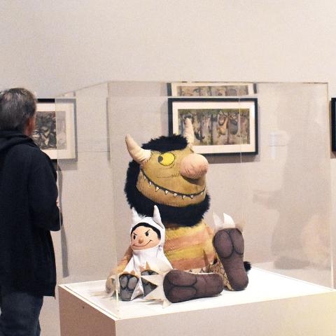 A stuffed monster and child in a monster costume in a case with a vitrine over them in a gallery setting.