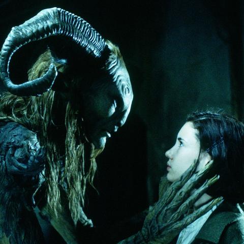 Still from the movie Pans Labyrinth showing the main character, Ofelia, standing face-to-face with a large, horned faun creature.