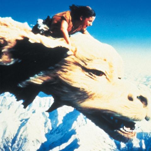 Still from the movie The NeverEnding Story showing the main character, Bastian, riding over snow capped mountains on the dragon Falkor.