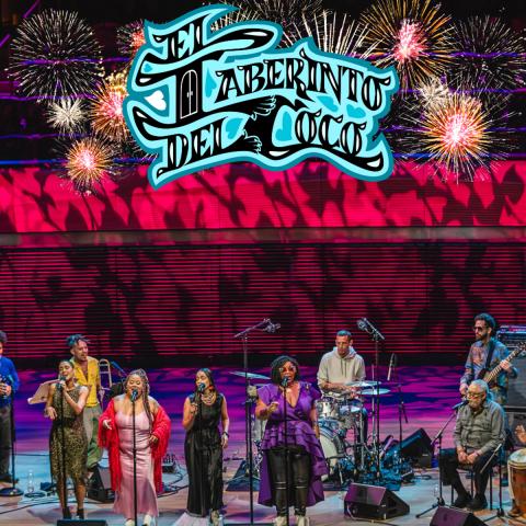 The band performs on a colorful stage with the name, El Laberinto del Coco in blue illuminated script above them.