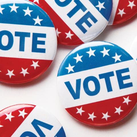 On a white table sits a collection of red, white, and blue buttons with the word Vote and stars printed on them.