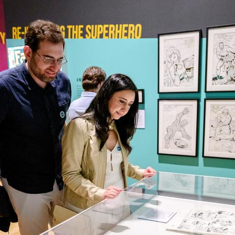 A man and a woman in a gallery look at a case with comic book art in it.