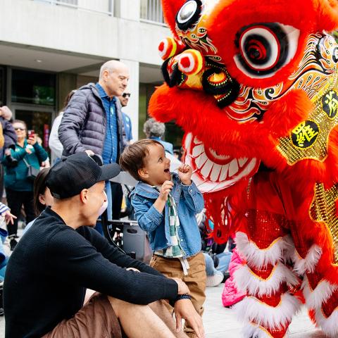 A child stares excitedly at a red dragon puppet in the courtyard.