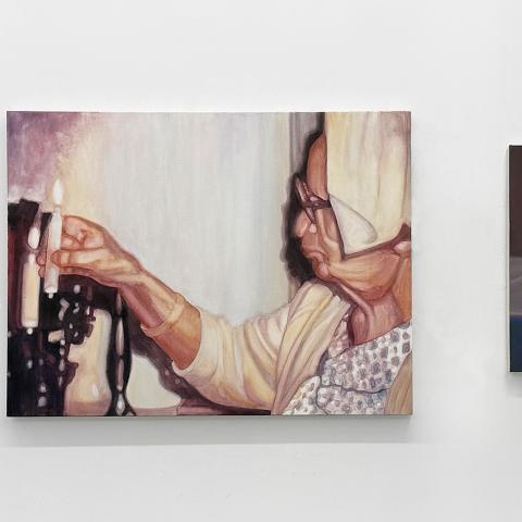 Three paintings on a gallery wall depicting candles with the one in the middle a person lighting one.