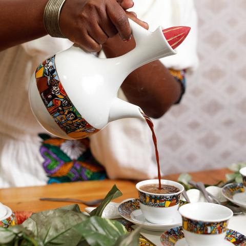 A close up of a person pouring coffee ceremonially in colorfully designed cups.