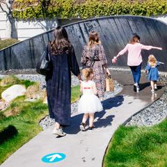 3 women and 2 girls walking on path through mist fountain