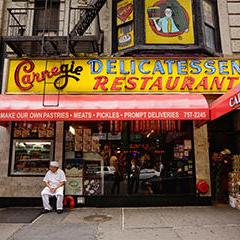 a man dressed as a cook sitting in front of Carnegie Deli