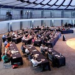 people seated at long tables listening to people seated on a stage