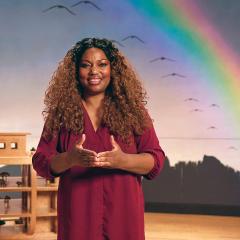 Noah's Ark educator standing in Noah's Ark exhibition with rainbow in the background smiling