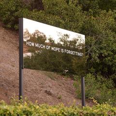 A large reflective signs outdoor on a hillside that says "How much of hope is forgetting?" by artist Chloe Bass