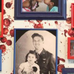 Various photographs of people framed in red and blue frames on a wall covered in wallpaper with a pattern of pomegranites