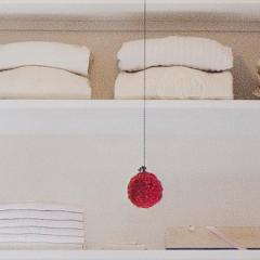 towels, perfume bottles and other items neatly arranged on shelves in a closet with a red ornament hanging on a string in front of them