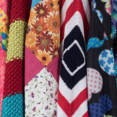 Eight colorful knitted blankets hung next to each other in a row