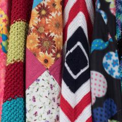 Eight colorful knitted blankets hung next to each other in a row