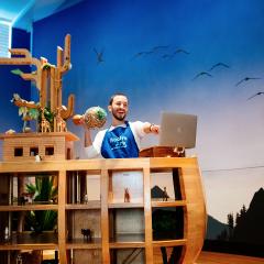 a Noah's Ark educator shaking a musical gourd telling a story to a computer screen from the Naoh's Ark gallery with a sky wallpaper and wooden ark.