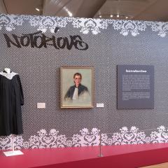 photo of the installation in the exhibition for Notorious RBG. It has a supreme court robe next to a portrait of Ruth Bater Ginsberg.