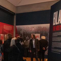 Photo of a group of people entering the gallery space of Blacklist: The Hollywood Red Scare. The title can be seen on a wall to the left.