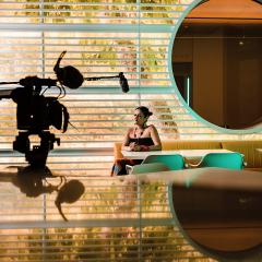 A women sits in the cafe ready for filming with a large film camera and a mic in front of her.