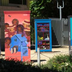 Four colorfully painted wooden boxes about 4 feet tall installed in a park.