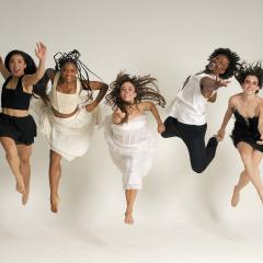 Seven dancers all facing forward and leaping into the air