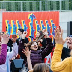 A group of people dancing outside in front of a large banner of a hanukkiah
