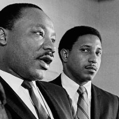 black-and-white photo of two African-American men dressed in suits and standing in front of microphones
