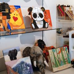 A store shelf with a close up of two wooden puzzles, a panda and a lion, and some books with a stuffed elephant below.