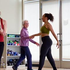 Five people of different ages, ethnicities, and genders dancing together in an exercise studio