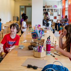 Art studio filled with young people and adults interacting around tables