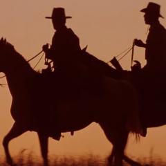 Silhouette of two cowboys riding horses against an orange sunset