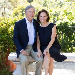 A man and woman sitting on a concrete bench with trees and foliage in the background